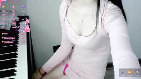 Media: Video of a young Asian woman with pale skin, long black hair, and a small chest, wearing a pink ribbed top and pink panties, sitting on a bed with a pink vibrator, surrounded by black sex toys.