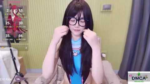 Media: Video of an East Asian woman with long black hair, wearing glasses, adjusting her hair, blue shirt, and beige couch in a yellow-wallpapered room.