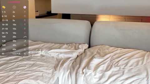 Media: Video of a modern, minimalist bedroom with white bedsheets and a beige headboard. The background features a wooden wall and a blurred kitchen area. A smartphone's screen overlay displays a map and icons, suggesting a virtual reality or augmented reality application.