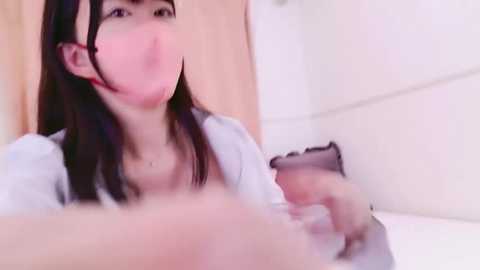 Media: A video of a young Asian woman with long black hair, wearing a white top, holding a phone while sitting in a bathtub, with blurred background showing a tiled wall.