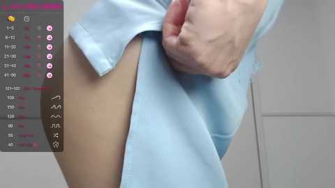 Media: Video of a hand lifting a blue hospital gown, revealing light-skinned buttocks, in a clinical setting with a gray door and a display showing temperature, heart rate, and blood pressure readings.