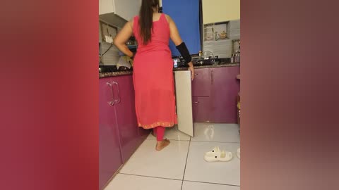 Media: Video of a woman in a pink sari and black wristbands standing in a modern kitchen with purple cabinets and white tiles.