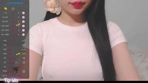 Media: A video of an Asian woman with long black hair and fair skin, wearing a tight white T-shirt, captured in a bedroom setting with a digital video recording overlay.