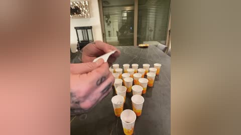 Media: Video of a man pouring beer into paper cups on a table, with a tattooed arm visible, in a modern, well-lit room with large windows and a dark countertop.