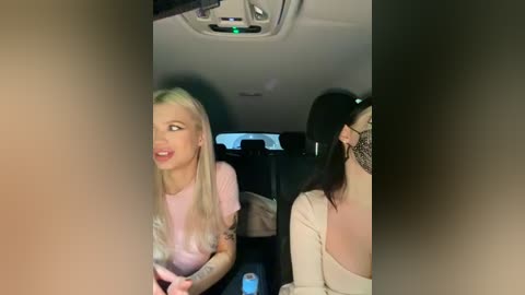 Media: Video of a blonde woman with tattoos and a pink shirt smiling inside a dimly lit car, with a tattooed woman in a white shirt sitting behind her.