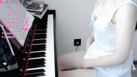 Media: Video of a fair-skinned woman in a white lace bra and panties, sitting at a grand piano with sheet music, playing, in a bright, modern room.