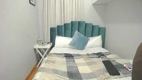 Media: Video of a modern bedroom with a teal upholstered headboard, white bedding, a blue pillow, a striped quilt, a nightstand, and a white curtain.