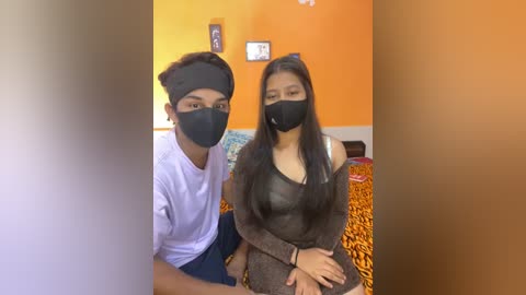 Media: Video of two young people, a boy and a girl, wearing black face masks, in a room with orange walls and leopard-print bedspread.