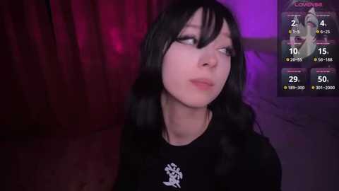 Media: Video of a pale-skinned woman with long black hair, wearing a black shirt, in a dimly lit room with purple and red lighting, showing a video game scoreboard in the background.