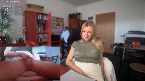 Media: A video captures a blonde woman in a green sweater and white skirt, holding a white paper in a cluttered office. A digital overlay shows a naked woman lying on a table.