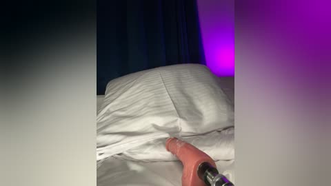 Media: A video of a person's hand holding a pink, realistic-looking dildo under a white sheet, with a purple light illuminating the background.