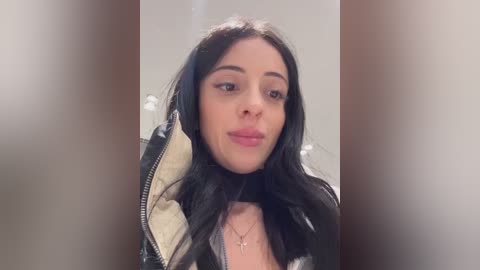 Media: Video of a young woman with long, straight black hair, fair skin, and a slight smile, wearing a black leather jacket and a necklace, against a blurred background.