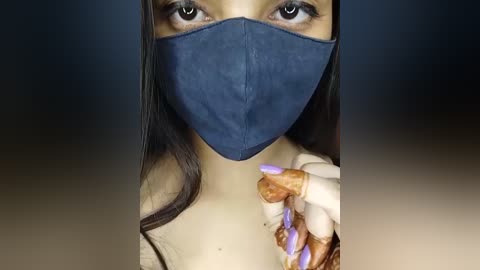 Media: Video of a woman with long, dark hair, wearing a blue surgical mask and a beige top, showcasing her manicured nails with lavender polish.