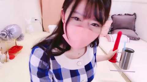 Media: Video of an East Asian woman with long black hair, wearing a blue and white checkered shirt, face mask, and holding a red broom, in a clean, modern kitchen.