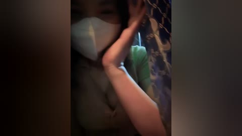 Media: A blurred, dimly-lit video of a person in a surgical mask, possibly a healthcare worker, holding a syringe against a dark, textured background.