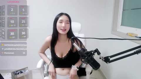 Media: Video of an East Asian woman with long black hair, wearing a black tank top, sitting in front of a camera and microphone in a modern studio.