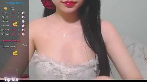 Media: Video of an Asian woman with fair skin and long black hair, wearing a white lace strapless dress, sitting indoors.