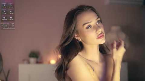 Media: Video of a young woman with long brown hair, fair skin, and red lipstick, wearing a gold necklace, in a dimly lit room with candles and potted plants.