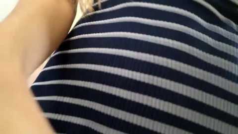 Media: A close-up video of a person's torso, showcasing their upper arm and shoulder, wearing a dark blue and white striped shirt. The texture of the fabric is slightly textured, giving a soft, ribbed appearance. The background is blurred, focusing attention on the shirt.