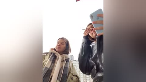 Media: Video of two people, a woman with long hair and a man with short hair, both in winter coats, taking a selfie in front of a blurred cityscape.