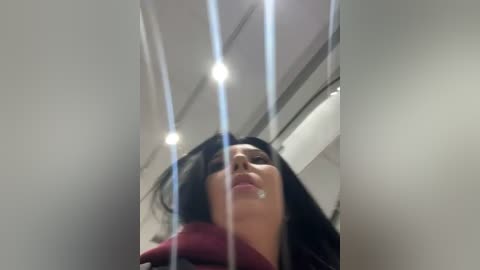 Media: Video of a woman with long black hair, wearing a red scarf, looking upward with a serene expression, in a modern, well-lit room with white walls and recessed lighting.