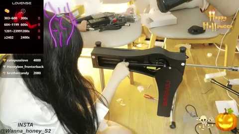 Media: Video of a woman with long black hair, wearing a white lab coat, assembling a black firearm on a table. The room is cluttered with tools and equipment.