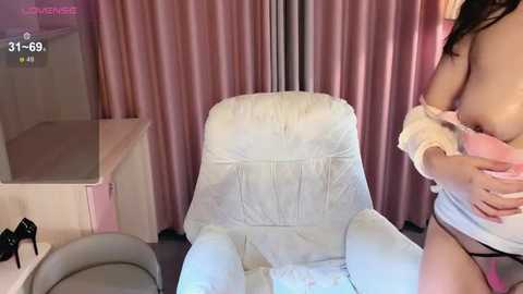 Media: Video of a woman in a pink room, partially undressed, holding her breast, wearing a white towel and black panties.