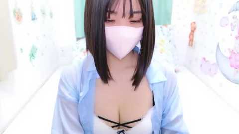 Media: Video of an Asian woman with short black hair, wearing a white mask, light blue blouse, and black lace bra, standing in a pastel-themed room with colorful decorations.