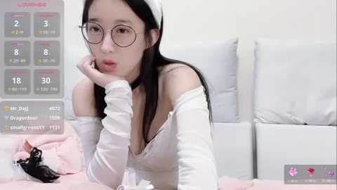 Media: Video of an East Asian woman with long black hair, wearing glasses and a white off-shoulder top, lying on a white bed, with a calendar overlay showing \"Mr. D's\" schedule.