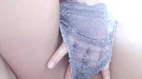 Media: Video of a close-up of a light-skinned person's thigh, partially covered in a delicate, lacy gray thong, with a hand gently touching the skin above the underwear.