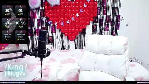 Media: Video of a plush white bed with pink heart-shaped pillows in a pink and black room, featuring a red heart-shaped wall and a black microphone stand.