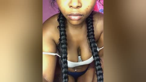 Media: Video of a Black woman with braided hair, wearing a white off-shoulder top, revealing cleavage and blue shorts, against a pink background.