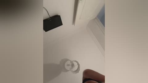 Media: A video of a ceiling with a black speaker mounted, reflecting on a shiny white surface below, and a hand holding a phone partially visible at the bottom.