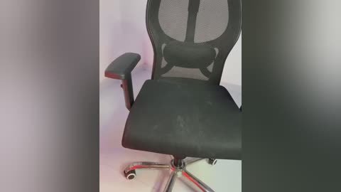 Media: Video of a black ergonomic mesh office chair with adjustable armrests, featuring a modern design with a silver base and caster wheels. The chair sits against a plain, light-colored background.