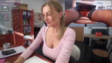 Media: A photo of a blonde woman in a pink top and black shorts, sitting at a desk, with a close-up of her crotch.