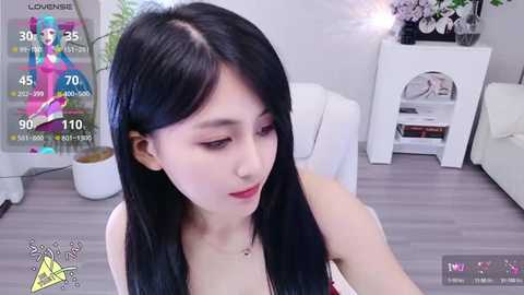 Media: A video of a young East Asian woman with long black hair and fair skin, wearing a red dress, taken in a modern living room with a white sofa and plants.