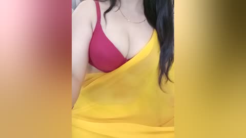 Media: A video of a woman in a red bra, covered partially by a yellow sari, with long dark hair. The background is blurred, with warm colors.