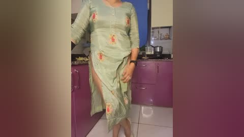 Media: Video of a woman in a green, floral-print sari, standing in a modern kitchen with purple cabinets, white countertops, and a blue window.