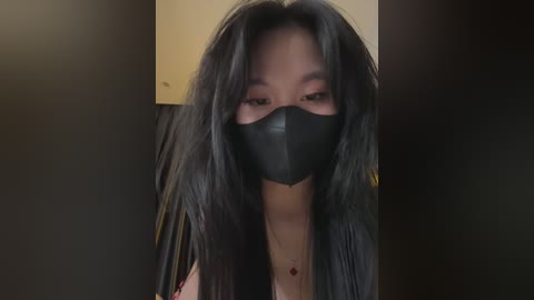 Media: Video of a young Asian woman with long black hair, wearing a black face mask and a black top, against a dimly lit background.