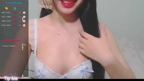 Media: Video of a young Asian woman with fair skin, long black hair, and red lipstick, wearing a white lace bra with light blue bows, smiling, with a \"Loomise\" watermark in the corner.