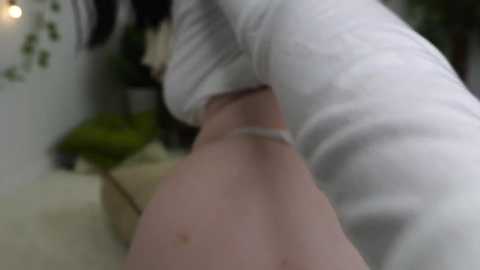 Media: Video of a person wearing white clothing, leaning over a person's thigh, with blurred background including plants and a wooden surface.