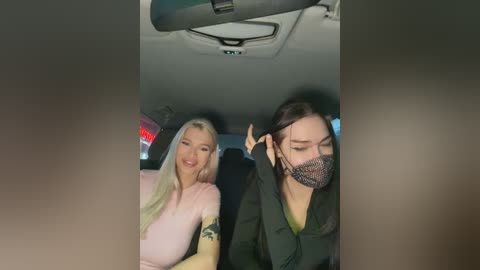 Media: A video captures two women in a car, one with blonde hair and a pink top, the other with dark hair, wearing a green jacket and face mask.