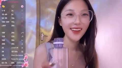 Media: Video of an Asian woman with long black hair, wearing glasses, smiling, holding a clear plastic cup, against a blurred indoor background, with a live streaming overlay showing her stats.