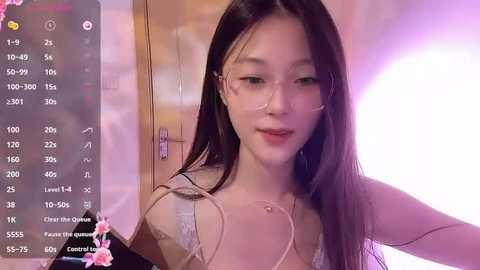 Media: A video of an Asian woman with long black hair, wearing a white lace bra, smiling, in a dimly lit room with pink lighting, holding a phone.