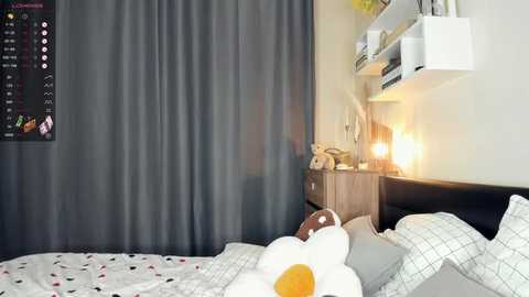 Media: A video of a modern, minimalist bedroom with a white bed adorned with a cloud-patterned duvet, a single orange balloon, and gray curtains. A wooden nightstand holds a lamp and a framed picture.