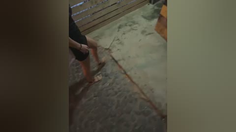 Media: A video of a partially obscured person in black shorts and a black shirt standing on a wet, grey concrete floor, with a metal railing visible in the background.