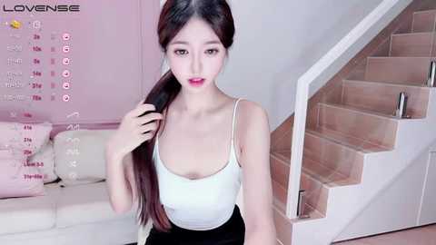 Media: Video of an East Asian woman with long black hair, wearing a white tank top and black skirt, posing in a modern, pastel-toned living room with a white couch and pink calendar.