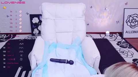 Media: Video of a woman in a white massage chair with a blue light, holding a black vibrator, in a room with floral and rose-themed decor.