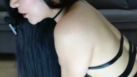 Media: Video of a woman with long black hair, fair skin, and a slender physique, wearing a black leather harness, seen from the side.