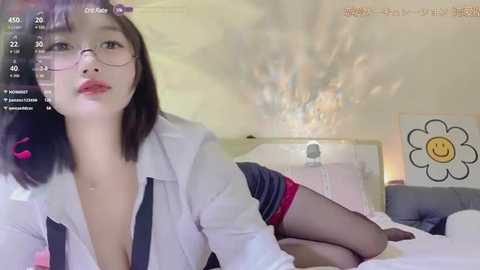 Media: Video of an East Asian woman with straight black hair, wearing glasses, a white blouse, black shorts, and red stockings, lying on a bed, in a bright, modern bedroom.